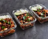 Meal prep für Muskelaufbau: Drei Glasbehälter mit Reis, schwarzen Bohnen, Hähnchen und Limette. Perfekte meal prep muskelaufbau rezepte für deine Fitnessziele.
