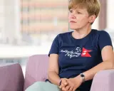 Monika Witkowska w granatowej koszulce z napisem "Odbudujmy Nepal" siedzi w różowym fotelu, patrząc w bok.