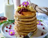 Pile de pancakes healthy garnis de bananes, grenades et fleurs roses. Un délice pour un petit-déjeuner sain.