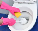 Hände in pinken Handschuhen reinigen die Toilette mit einer Bürste und einem Schwamm. Soda ist ein tolles Hausmittel zur Toilette mit Soda reinigen.