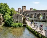 Un pittoresco borghetto sul Mincio con mulini ad acqua, un ponte ad archi e persone che passeggiano e pedalano.