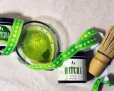 Zielony napój matcha w szklance, obok dwa słoiczki z napisem "MATCHA ORGANICZNA" i miarka krawiecka. Matcha co to? To zdrowy napój.