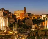 Antike Ruinen des Forum Romanum in Rom bei Nacht. Der Kolosseum und ein Triumphbogen sind beleuchtet.