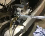 Klucz nasadowy odkręca odpowietrznik zacisku hamulcowego motocykla, podczas gdy przez przezroczysty wężyk płynie płyn. To etap wymiany płynu hamulcowego.