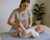 Fizjoterapeuta niemowlęcy delikatnie masuje nóżki dziecka leżącego na macie.
