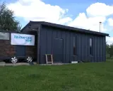 Mobilny garaż bez pozwolenia, z napisem "Zbuduj sam dom", stoi na trawie.