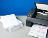 Stos białego papieru obok drukarki, która drukuje dokument. Różne rodzaje papieru czekają na użycie.