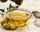 Aceite de oliva virgen extra vertiéndose en un cuenco, con aceitunas y utensilios de cocina. Sus características lo hacen ideal.