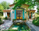 Encantadoras fachadas de casas rústicas con contraventanas turquesas y un estanque rodeado de flores.