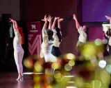 Tancerki w jasnych bluzkach i białych spodniach wykonują zmysłowy taniec. Ich dłonie unoszą się w powietrzu, tworząc dynamiczną choreografię. To piękny pokaz bachata solo.