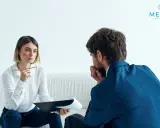 Kobieta z notatkami i mężczyzna w garniturze rozmawiają. Tak wygląda psychoterapia: wsparcie i zrozumienie w trudnych chwilach.
