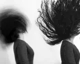 Dos cabezas con cabello largo y oscuro en movimiento, capturadas con un obturador fotográfico que crea un efecto de desenfoque dinámico.