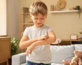 Niño con varicela en brazos y cara, rascándose el brazo.