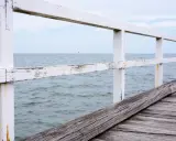 Drewniane molo we Władysławowie z białą, przetartą balustradą i widokiem na spokojne morze.