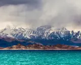 Turkusowe jezioro w kotlinie kaszgarskiej, otoczone surowymi, skalistymi wzgórzami i ośnieżonymi szczytami gór.