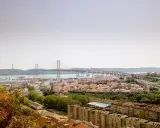 Blick auf Lissabon mit der Hängebrücke und dem Cristo Rei Denkmal. Im Vordergrund die Dächer von Häusern, die an den "Cemitério dos Prazeres" erinnern.