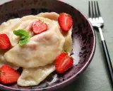 Pyszne pierogi z truskawkami, udekorowane świeżymi owocami i miętą, czekają w misce na widelcu.