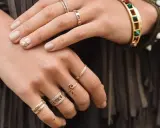 Mani adornate con anelli, tra cui uno con numeri romani, un bracciale colorato e un anello a forma di "S". Non c'è un anello da single specifico, ma la varietà suggerisce stile personale.
