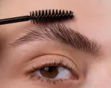 Une brosse à cils peigne les sourcils d'une femme pour les mettre en forme.