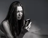 Ragazza piange guardando il telefono, vittima di revenge porn. La legge punisce chi diffonde immagini private senza consenso.