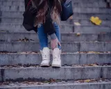 Kobieta w beżowych botkach na schodach, otoczona jesiennymi liśćmi.