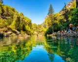 Un refrescante charco del aceite, rodeado de vegetación exuberante y rocas, con gente disfrutando del día.