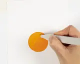 En hand håller en grå tuschpenna och målar en orange cirkel på vitt papper.