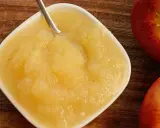 Frisches Apfelmus mit Schale, zubereitet im Thermomix, in einer weißen Schale auf Holzuntergrund. Daneben liegen zwei rote Äpfel.