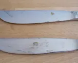 Zwei Messer mit deutlichen Rostflecken auf dem Besteck liegen auf einem Holztisch.