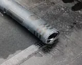 Rolka papy na zimno leży na mokrym dachu. Widać fragmenty wzoru na papie i jej zwinięty koniec.