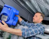 Un technicien installe un nouveau bloc VMC. L'entretien vmc obligatoire garantit un air sain dans votre logement.