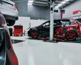 Taller con coches modificados. Uno negro con diseño de hexágonos rojos y llantas rojas, otro negro y rojo con alerón. Se pregunta cuánto cuesta reprogramar un coche.