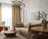 Nowoczesny salon szaro beżowy z wygodną kanapą, puszystym fotelem i drewnianymi meblami.