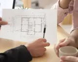 Architekt omawia z klientami projekt domu, wskazując na planowaną powierzchnię netto budynku.