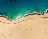 Luftaufnahme eines einsamen **Surferstrands** auf **Fuerteventura**. Türkisblaues Meer trifft auf goldgelben Sand und eine felsige Küste. Eine Straße schlängelt sich entlang der Küste.