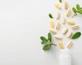Kapsułki z lactobacillus plantarum rozsypują się z białej buteleczki, otoczone zielonymi listkami.
