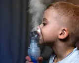 Chłopiec z maską inhalacyjną na twarzy, wdycha parę. Skuteczna inhalacja na katar u dziecka.