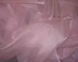 A shimmering pink organza fabric, with its sheer, crisp texture, drapes elegantly, catching the light.