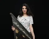 Une musicienne tient un kanoun, instrument de musique à cordes pincées, devant un fond noir.