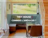 Aménagement d'un **tiny house interieur** : un espace cosy avec lit, bureau et vue sur la nature.