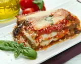 Una fetta di parmigiana di mare pugliese, con melanzane, pomodoro e mozzarella filante, guarnita con basilico fresco.
