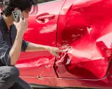 Hombre llama por teléfono señalando el grave golpe en la puerta de su coche rojo.