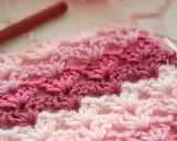 Tejido a crochet con hilo rosa y blanco. Un patrón de chaleco fácil en progreso, con un ganchillo rojo al fondo.