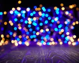 Luci blu e dorate creano un magico effetto bokeh su uno sfondo scuro, con un piano in legno in primo piano.