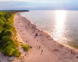 Piękna plaża z lasem sosnowym, idealne miejsce, gdzie pojechać na wakacje w Polsce. Słońce odbija się w wodzie, a ludzie odpoczywają na piasku.