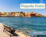 Słoneczna pogoda na Krecie w lipcu. Widok na port z kolorowymi kamienicami i ławką nad turkusową wodą.