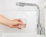 Main tenant rempli un verre d'eau sous un robinet de cuisine moderne, peut-être pour tester un nouveau joint mitigeur cuisine.