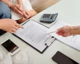 Des mains examinent un contrat de bail verbal, avec un téléphone, une calculatrice et une théière à proximité.