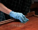 Mano enguantada lijando superficie de madera barnizada. El lijado es un paso clave para aplicar lac.