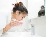 Une jeune femme se lave le visage le matin, sous un jet d'eau fraîche. Une routine beauté essentielle pour se réveiller.